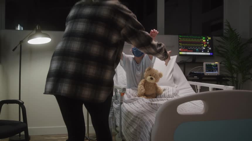 Mother hugging her daughter who is sitting on the bed in a hospital room