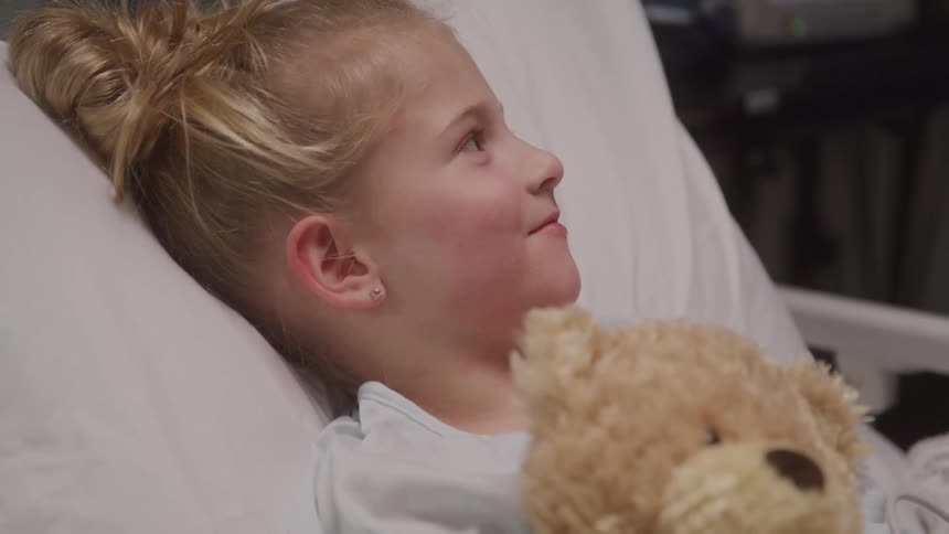 Little girl with a teddy bear lying in a hospital bed