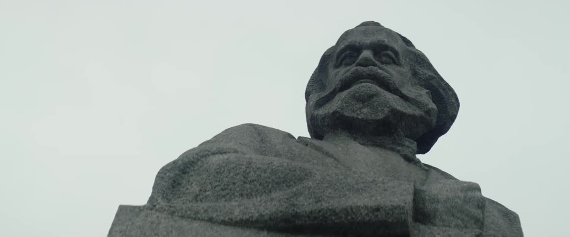 A stone bust of a man sits under overcast skies