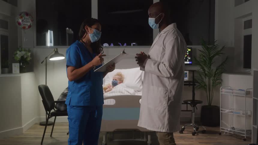 Nurse and doctor discuss beside hospital bed with patient
