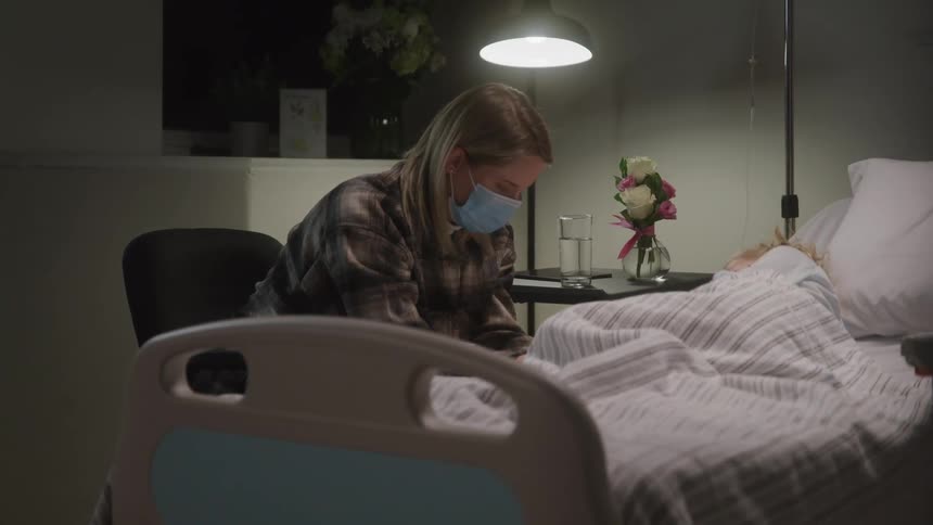 Mother sitting next to her daughter who is sleeping in a hospital bed
