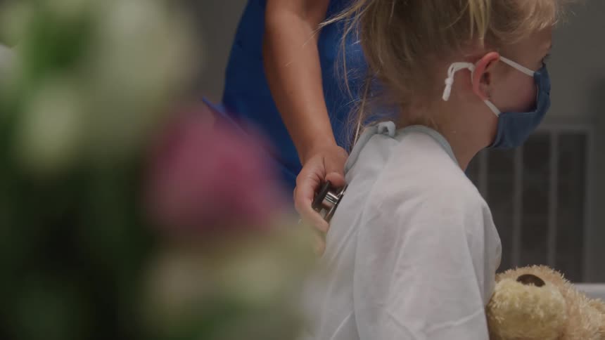 Nurse checking the breathing of a little blonde girl sitting on a hospital bed