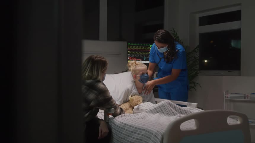 Nurse consulting a little girl sitting on a hospital bed with her mother