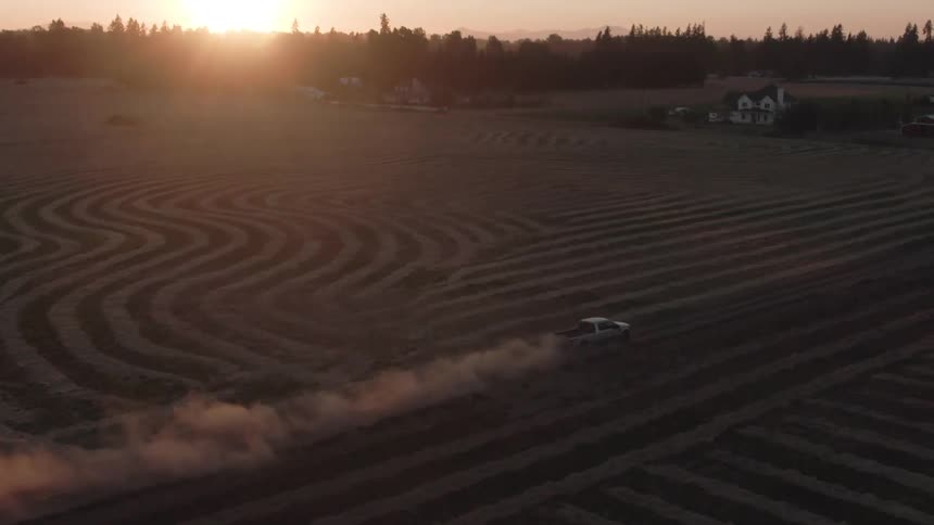 A truck drives along a field at dusk