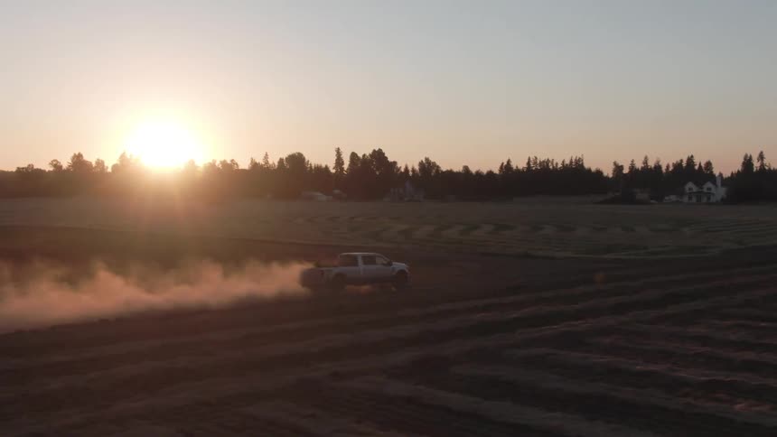 A truck drives along a field at dusk