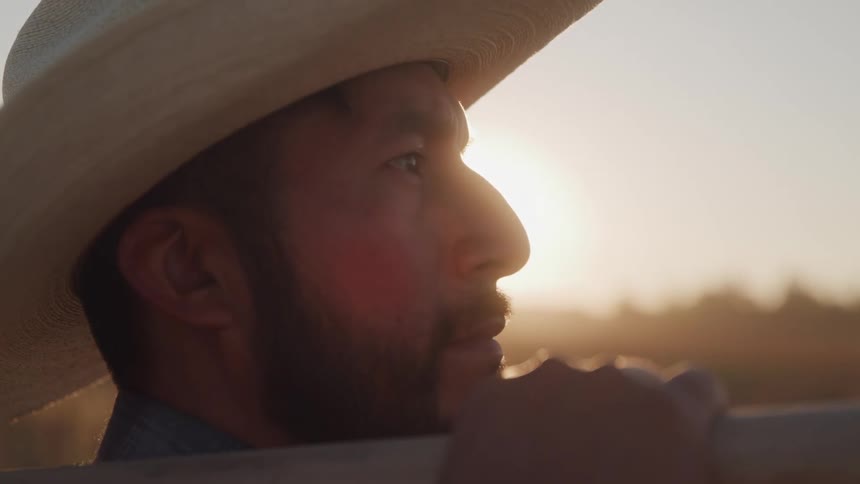 Bearded man with hat outdoors at dawn with a wooden handle on his shoulder