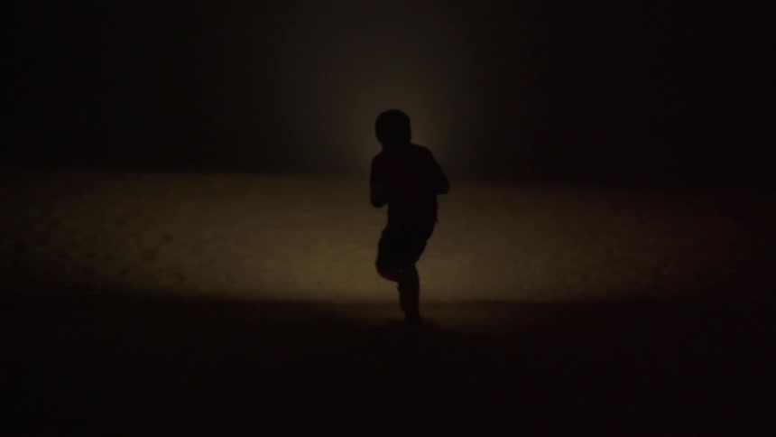 A person running in a dark area towards water
