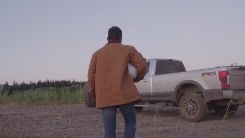A man walks towards a parked pickup truck on a road outdoors during daytime