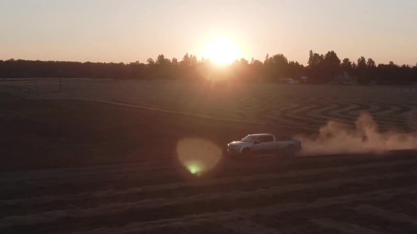 A truck drives along a field at dusk