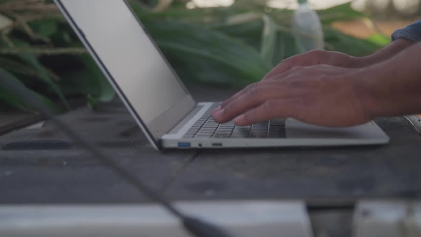 Close up of a man typing on a laptop outdoors during daytime