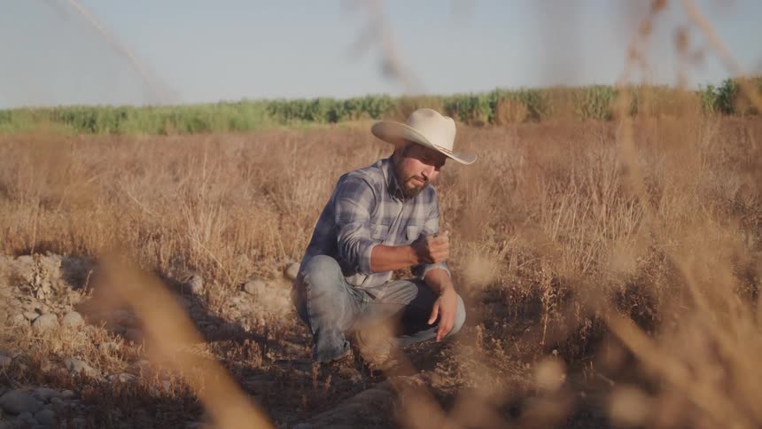 A man picks up some dirt and then slowly lets it fall back to the ground