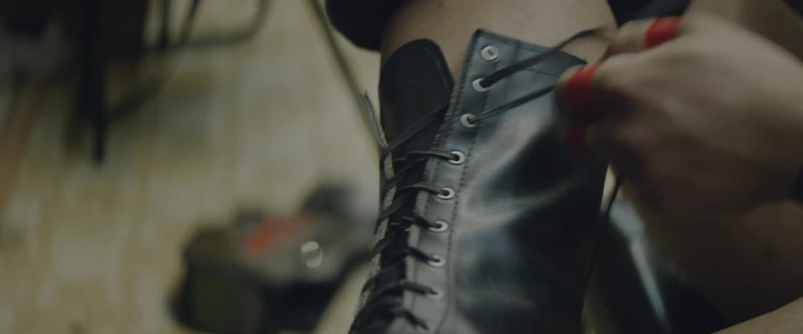 A person with tape on their hands is lacing up their boot