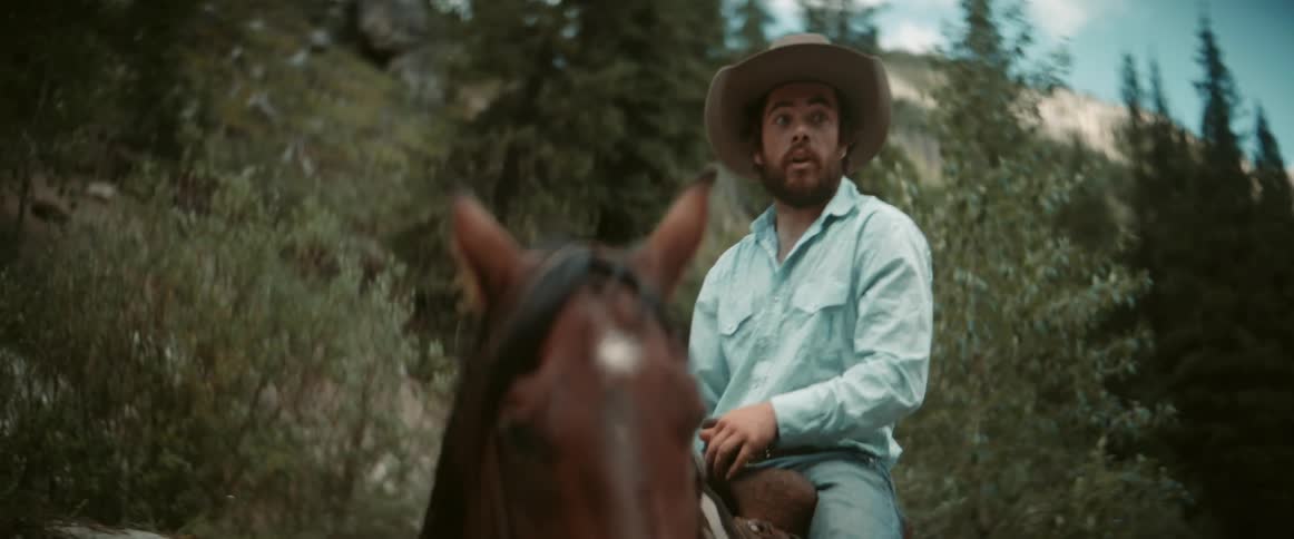 A man jumps off a horse holding a yellow whip in the woods at midday