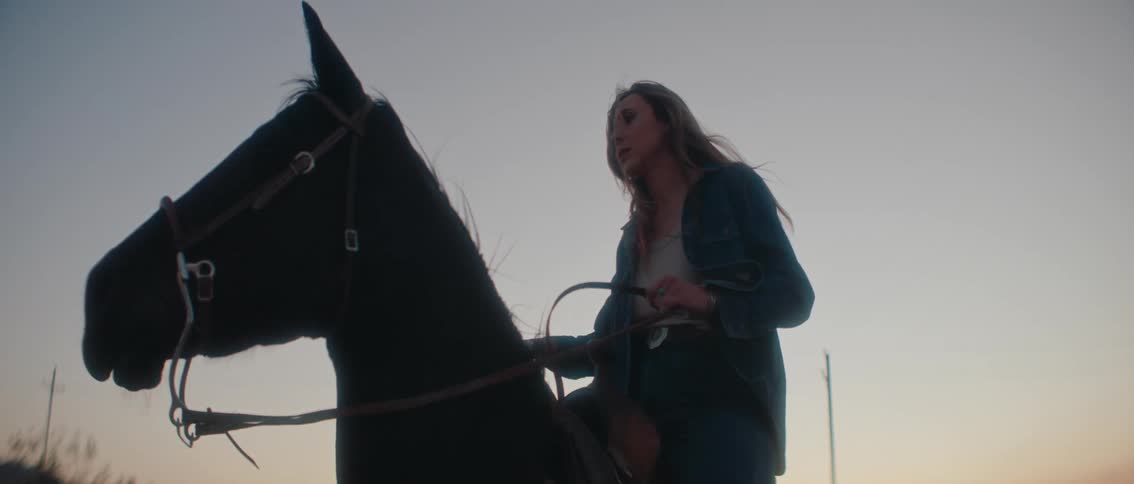 A contemplative shot of a woman on horseback against a soft outdoor backdrop at dusk