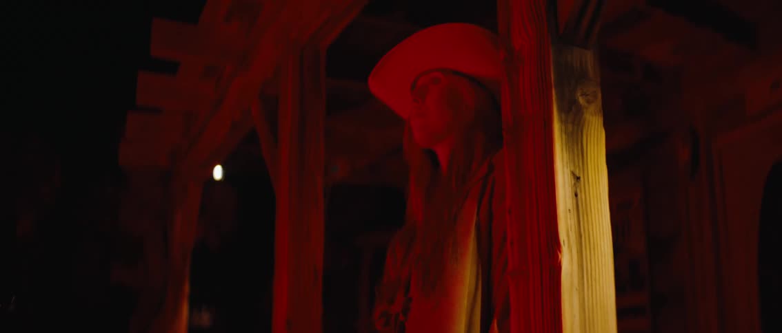 A person wearing a cowboy hat is captured in a dark dimly lit setting illuminated by a striking red light the scenes intense lighting creates a dramatic and somewhat mysterious ambiance