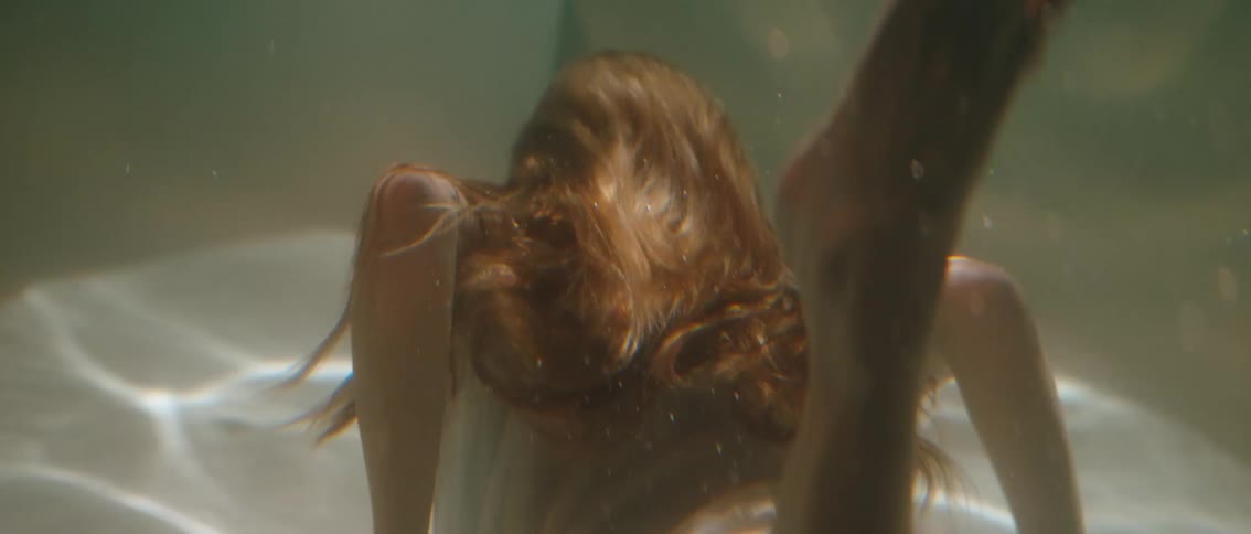 A person with long flowing brown hair is submerged underwater with bubbles rising around them the scene is serene with light filtering through the water creating a dreamlike quality