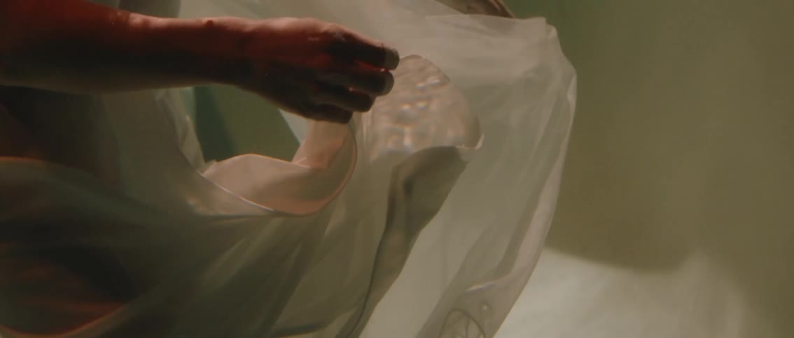 A person is shown submerged in water wearing a white dress with both hands reaching out and manipulating the fabric creating graceful movements the scene is bathed in a soft ethereal light enhancing the dreamlike and fluid imagery
