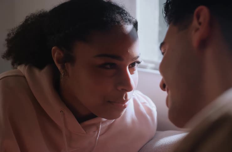A young couple is looking at each other affectionately in a closeup shot the woman smiles softly as she gazes at the man who is looking back at her