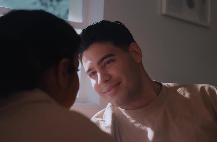 A closeup overtheshoulder shot of a man smiling warmly at a woman with his face in sharp focus as they have an intimate conversation in a sunlit room
