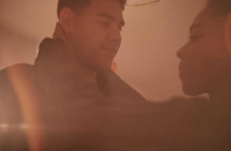 Smiling couple slow dances while sunlight glares through a window