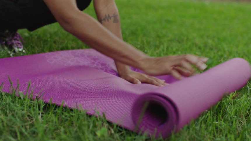 A woman unrolls a yoga mat in a park