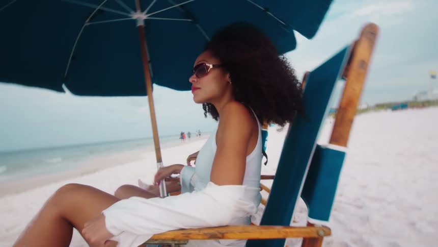 A woman sits on a chair on the beach next to a man in front of the ocean
