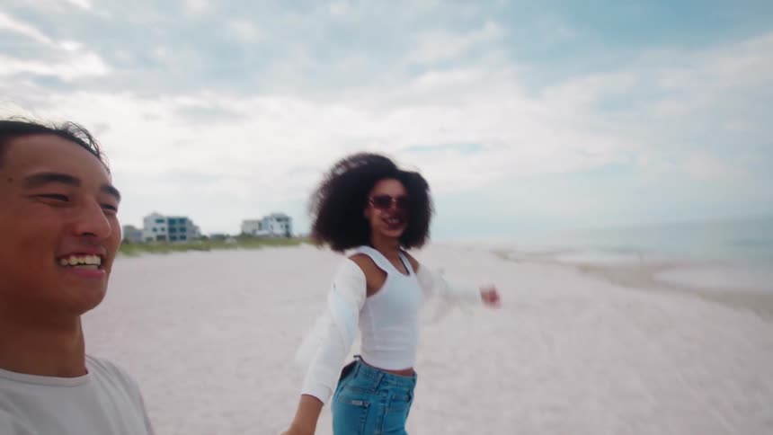 A couple having fun on the beach holding hands with the woman wearing sunglasses