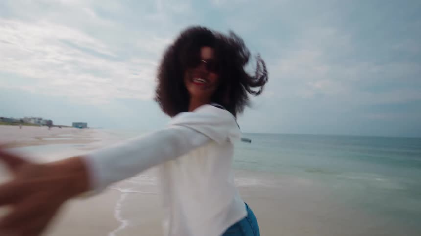A young black woman runs and spin while having fun outdoors at the beach during daytime