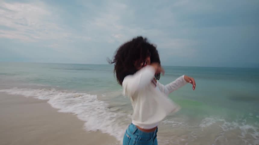 Woman with curly hair running happily on the beach