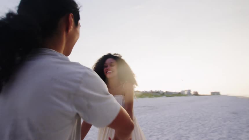 A couple dances playfully together on a sandy beach