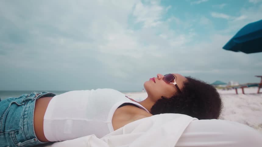 A young woman wearing sunglasses lying on the beach sand at midday