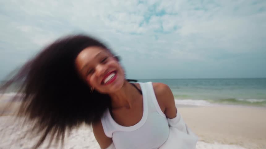 Curly haired woman with happy expression blowing a kiss while standing on the beach