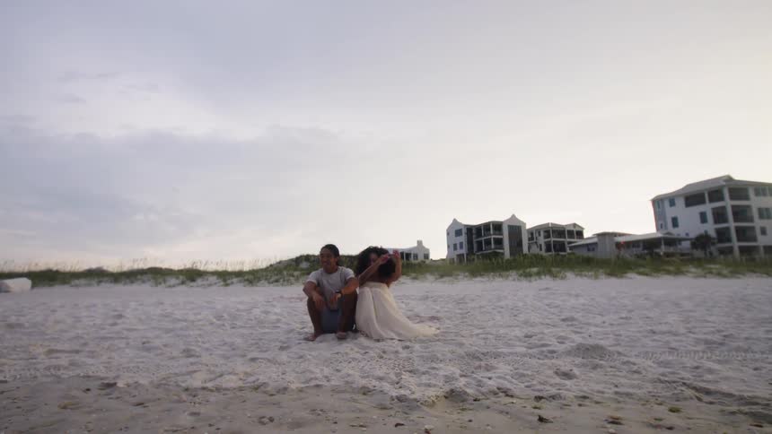 Man and a woman holding hands and sitting on the sand at the beach