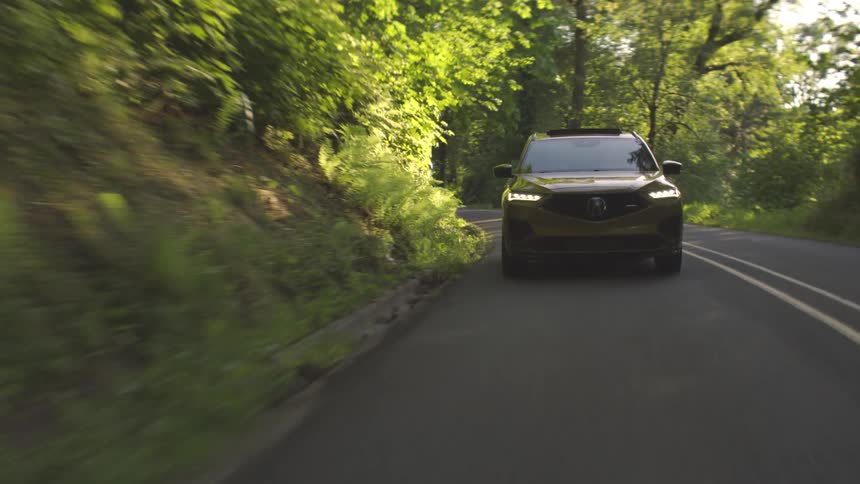 A sedan car driving on the freeway with tall trees lining each side of the road at midday