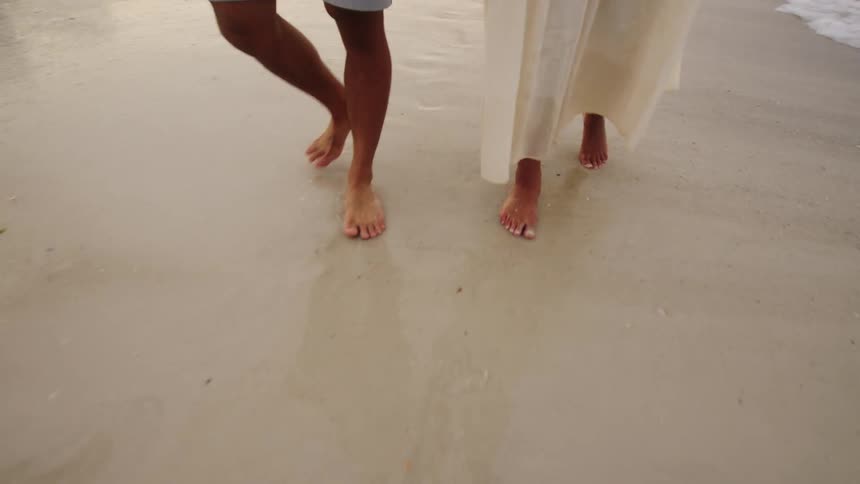 Two people walk barefoot at the shoreline