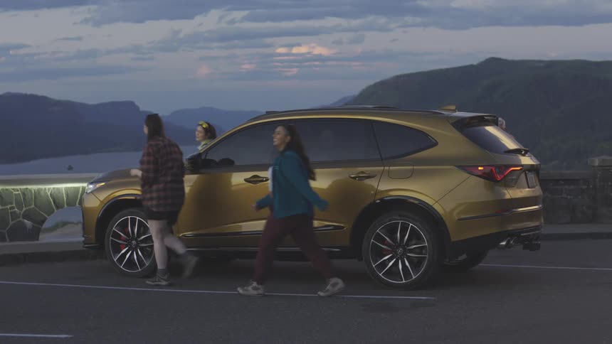 Three women exiting a parked suv in front of a landscape of mountains and sea