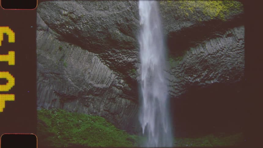 A single stream of water falls down a tall moss covered rocky cliff splashing into a pool at the bottom where a person is briefly visible