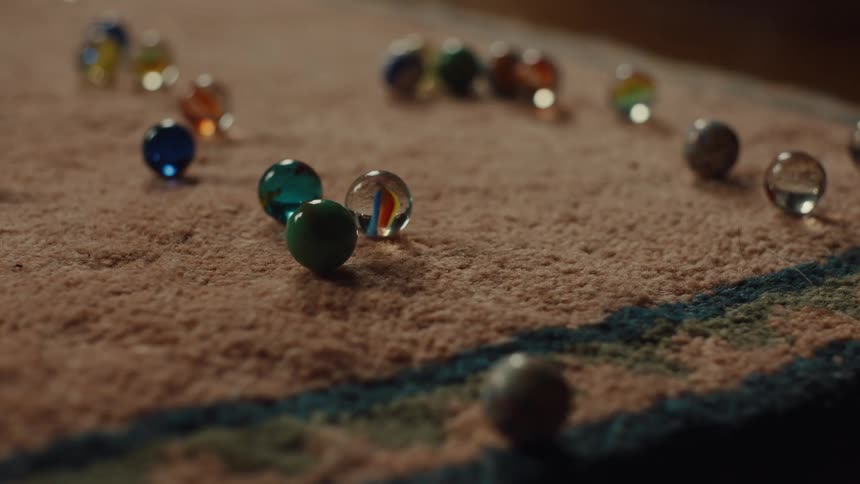 A persons hand throwing marbles onto a rug where several marbles are already lying
