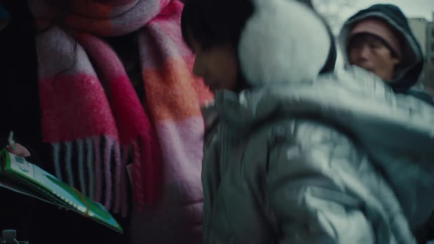 The video shows two people on a city street one person a young girl is wearing a silver puffer jacket and white fluffy earmuffs the other person is wearing a pink white and red striped scarf