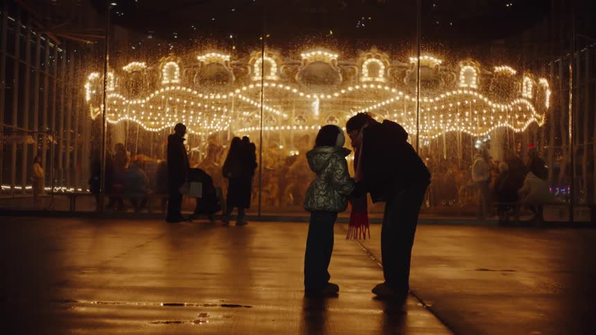 A mother and daughter hugging in front of a carousel ride at an amusement park