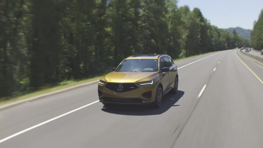 A gold car driving on a freeway with trees on both sides at midday