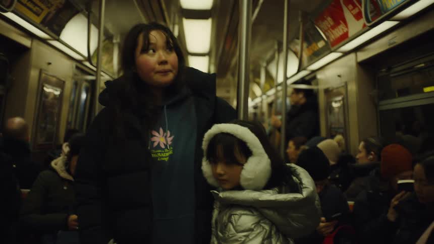 Asian woman and girl dressed warmly riding in a subway car the woman looks worried and the girl is staring at the floor with no emotionthe subway car is full of people also dressed warmly and sitting in seats
