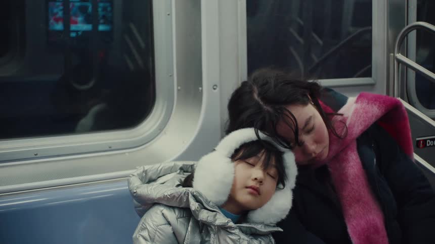 A woman sitting beside her son both wearing winter jackets sleeping during a train ride at night