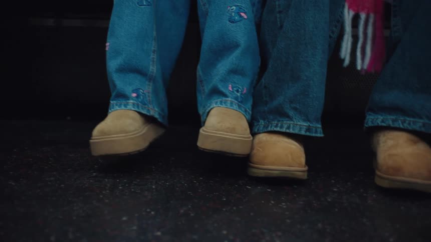 The legs and feet of two children wearing blue jeans and tan shoes on a dark reflective floor