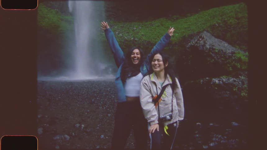 Two women pose smiling in front of a waterfall