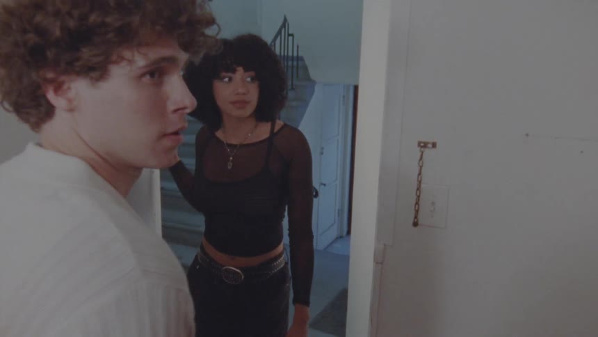 A young adult man opens the door for a young adult woman who enters the apartment the man appears nervous
