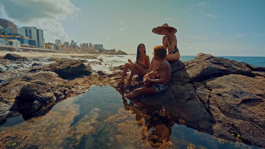 The video shows a group of people sitting on rocks by the ocean there is a watermark in the video that reads filmsupply there is no other text visible