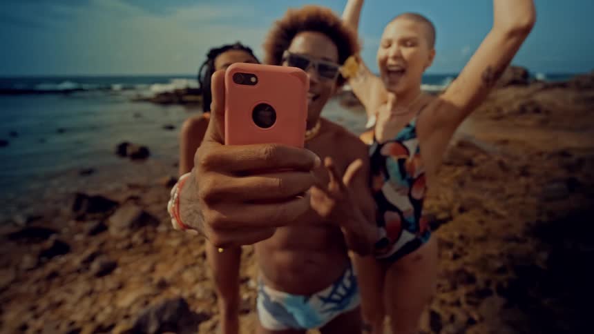 Three friends pose joyfully for a selfie on a rocky beach their expressions vibrant and full of energy