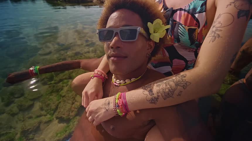 Two friends relax in the water wearing sunglasses colorful bracelets and visible tattoos