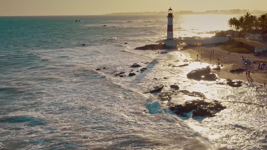 Lighthouse on rocky coast at sunset with crashing waves